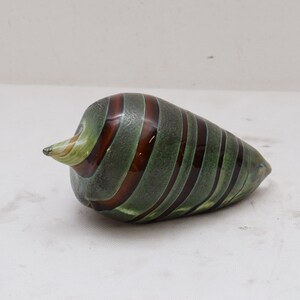 May include: A green and brown glass sculpture shaped like a seashell. The sculpture has a swirl pattern and is made of glass.