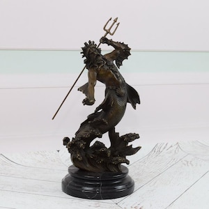 Puede incluir: Estatua de bronce de una criatura marina m&iacute;tica, posiblemente Poseid&oacute;n o Neptuno, sosteniendo un tridente. La escultura presenta intrincados detalles del rostro, el cabello y el cuerpo de la figura, montada sobre una base de m&aacute;rmol negro. Es un art&iacute;culo decorativo.