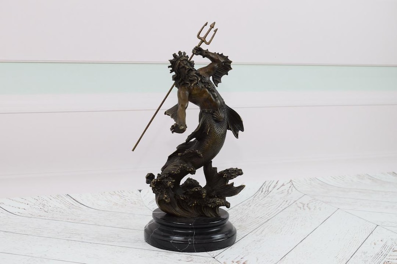Puede incluir: Estatua de bronce de una criatura marina m&iacute;tica, posiblemente Poseid&oacute;n o Neptuno, sosteniendo un tridente. La escultura presenta intrincados detalles del rostro, el cabello y el cuerpo de la figura, montada sobre una base de m&aacute;rmol negro. Es un art&iacute;culo decorativo.