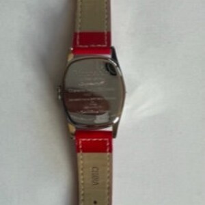 May include: A silver wristwatch with a red leather band. The watch face is oval shaped and the band has a silver buckle.