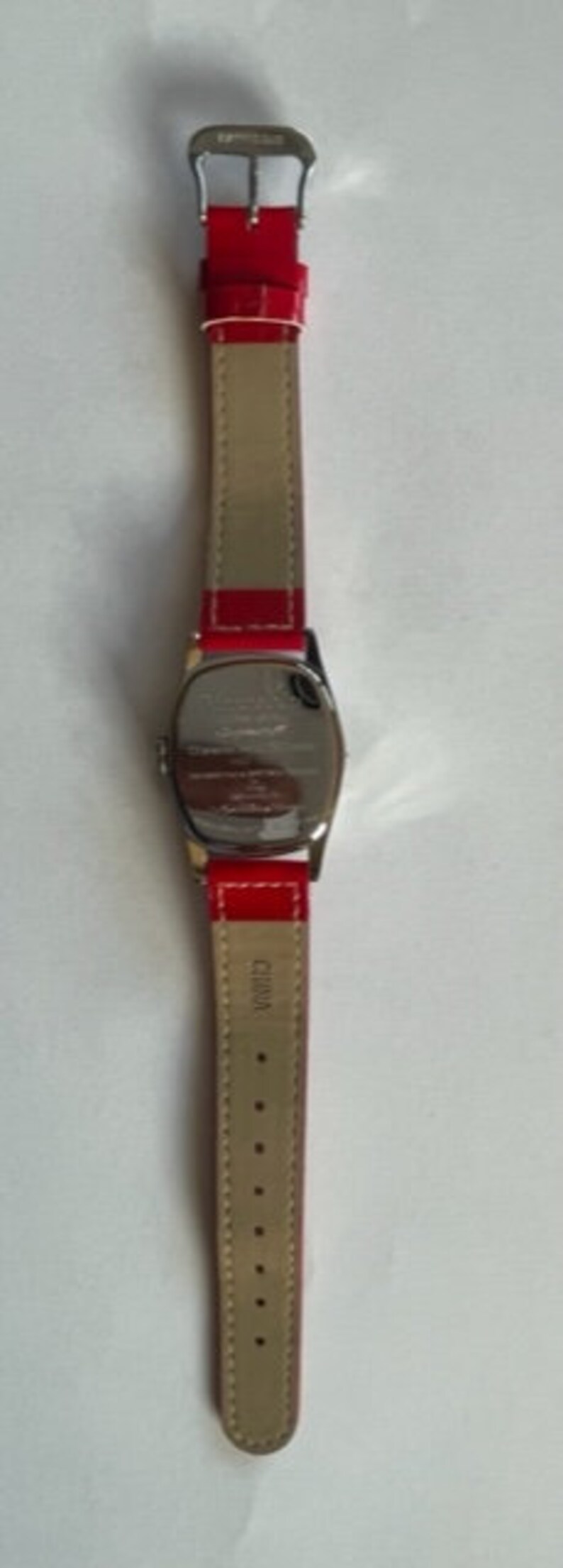 May include: A silver wristwatch with a red leather band. The watch face is oval shaped and the band has a silver buckle.