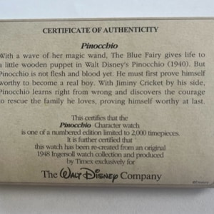 May include: A certificate of authenticity for a limited edition Pinocchio character watch. The certificate is printed on brown paper with a wood grain texture. The text states that the watch is one of 2,000 timepieces and was re-created from an original 1948 Ingersoll watch collection. The certificate is signed by The Walt Disney Company.