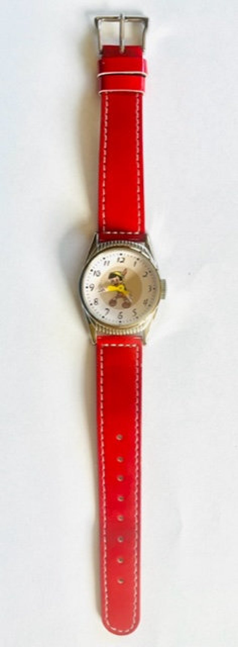 May include: A red leather wristwatch with a white face and black numbers. The watch face features a cartoon character with a yellow hat.