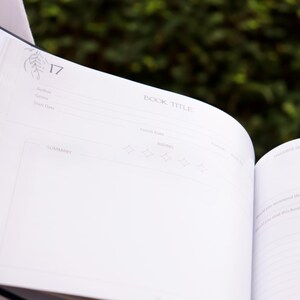 May include: A white book with a blue spine. The book is open to page 17, which has a section for recording book details, including author, genre, and a summary. The page also includes a rating section with five stars.