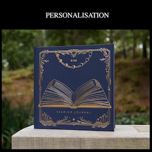May include: A navy blue reading journal with gold foil accents. The cover features a stylized illustration of an open book with a decorative border and the words "Reading Journal".