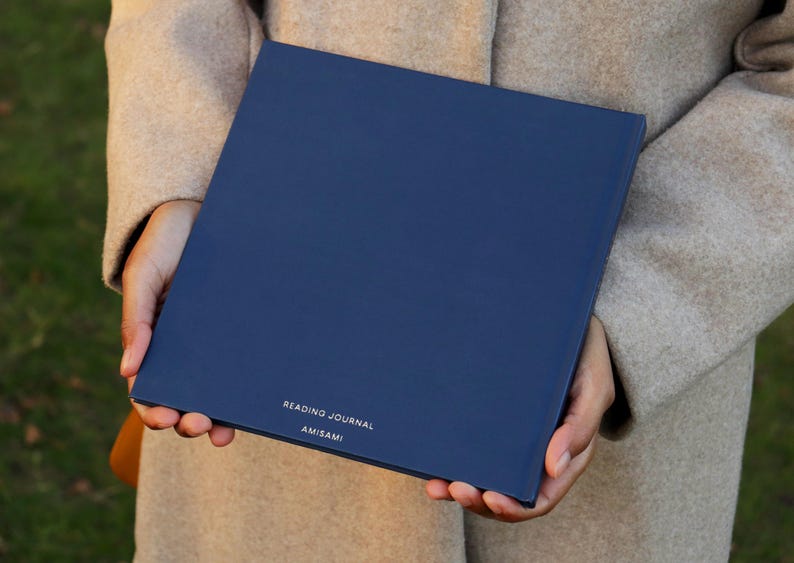 May include: A navy blue reading journal with the text "READING JOURNAL" and "AMISAMI" printed in white on the front cover.