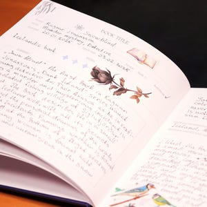 May include: Open book with a black rose illustration and handwritten text. The text includes the book title "Snow Blind" and the author's name "Ragnar Jonasson".