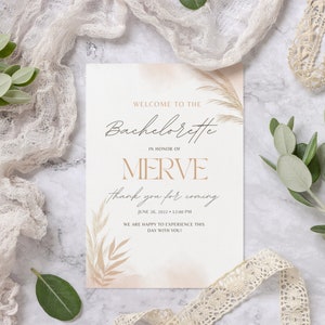 Könnte beinhalten: Ein Willkommenszeichen für einen Junggesellinnenabschied mit Aquarellhintergrund und Pampasgras. Das Schild lautet "Willkommen zur Bachelorette zu Ehren von Merve Vielen Dank für Ihr Kommen 26. Juni 2022 + 12:00 Uhr Wir freuen uns, diesen Tag mit Ihnen zu erleben!"