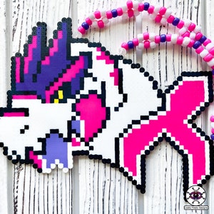 May include: A white, pink, purple and black perler bead artwork of a mythical creature with a large head and a long tail. The creature has a large, open mouth with sharp teeth. The bead art is hanging from a white and purple beaded necklace.