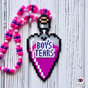 Peut inclure: Un collier de perles roses et violettes avec un pendentif en forme de cœur qui dit "Boy's Tears". Le pendentif est une image pixélisée d'une fiole de potion.