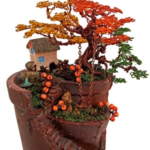 May include: A miniature wire tree sculpture featuring a small house, a swing, and orange beads. The tree has copper wire branches with gold and orange leaves. The sculpture is set in a brown ceramic pot.
