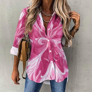 May include: A button-down shirt with a vibrant pink and white abstract pattern. The shirt has three-quarter sleeves with white cuffs and a classic collar. The shirt is paired with blue jeans.