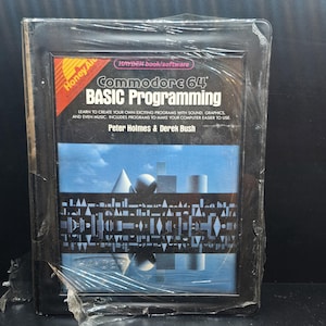 May include: A Commodore 64 BASIC Programming book, still in its original plastic wrap. The cover features geometric shapes against a blue sky background. The book is by Peter Holmes & Derek Bush.