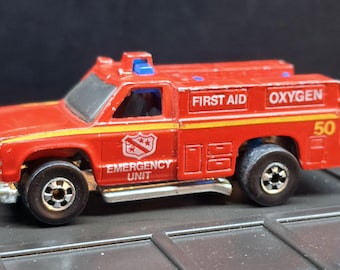 Könnte beinhalten: Ein rotes Notfall-Einsatzfahrzeug als Spielzeugauto aus Metall mit blauem Licht auf dem Dach, schwarzen Rädern und weißer Aufschrift FIRST AID, OXYGEN und EMERGENCY UNIT. An der Seite befindet sich ein Wappen und die gelbe Nummer 50.
