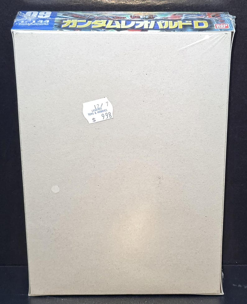 May include: A rectangular cardboard model kit box wrapped in clear plastic. The top edge features blue and white text including the Japanese characters ガンダムレオパルドD and the number 09. A small white circular price sticker is attached to the front.