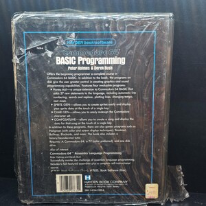 K&ouml;nnte beinhalten: Ein Commodore 64 BASIC Programmierbuch von Peter Holmes und Derek Bush, in Plastik versiegelt. Das Cover zeigt den Titel in gro&szlig;en wei&szlig;en Buchstaben, mit einer Beschreibung des Inhalts und der Funktionen des Buches.