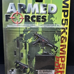 Puede incluir: Un juego de juguetes con metralletas MP5K negras en miniatura, cargadores y un maletín, empaquetado en una tarjeta verde y con estampado de camuflaje. El embalaje dice "ARMED FORCES" e incluye una advertencia sobre piezas pequeñas.