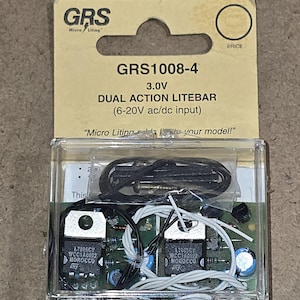 May include: A clear plastic box containing a GRS 1008-4 3.0V Dual Action Litebar with a 6-20V ac/dc input. The box includes a circuit board with two integrated circuits, wires, and a small black component.