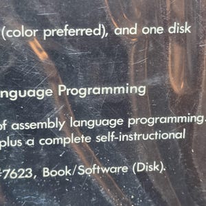 K&ouml;nnte beinhalten: Nahaufnahme einer dunklen Oberfl&auml;che mit wei&szlig;em Text. Der Text enth&auml;lt "(color preferred), and one disk", "language Programming" und "assembly language programming". Der Artikel ist als Buch/Software (Disk) gekennzeichnet.