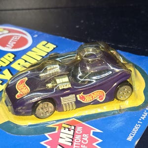 May include: Purple Hot Wheels car keychain with clear plastic top. The car has the Hot Wheels logo in red and yellow. The keychain is on a blue and yellow card that says "UP KEY RING".