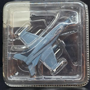 May include: A gray F-18 Hornet model airplane in a clear plastic package. The model has detailed wings, tail, and cockpit features. The packaging is sealed, suggesting a new, unopened product.