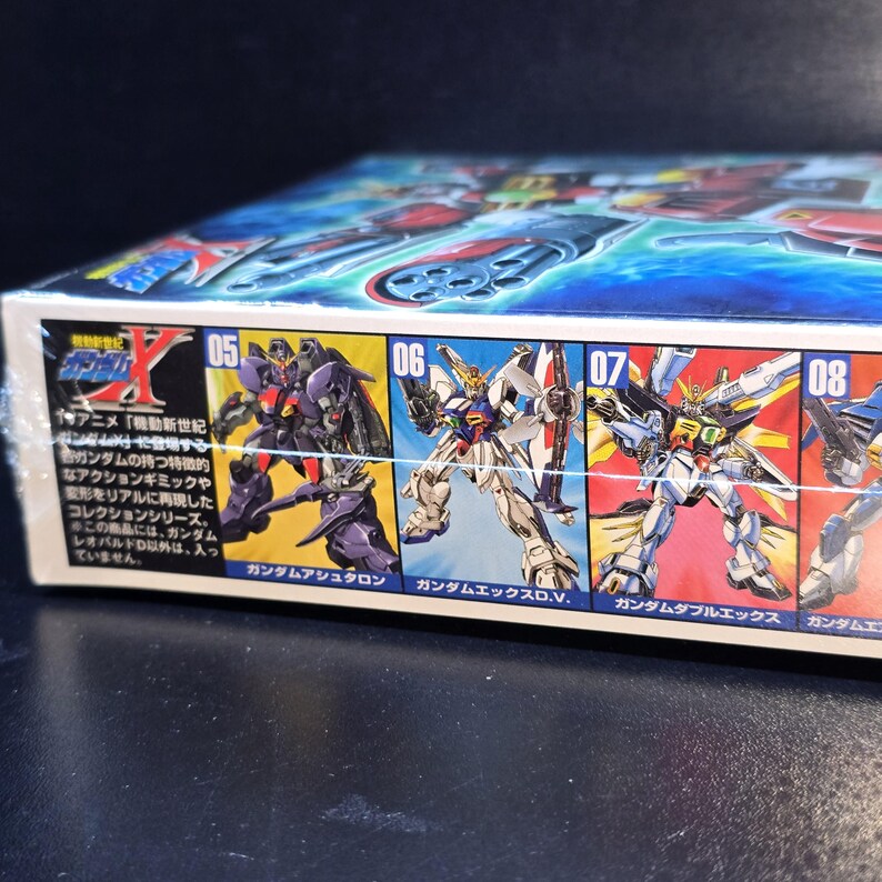 May include: A rectangular model kit box featuring illustrations of various Gundam robot figures labeled with numbers 05, 06, 07, and 08. The packaging displays Japanese text and colorful character art against a blue background, showcasing mechanical designs.