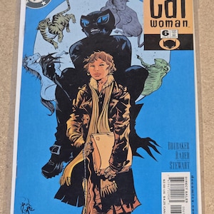 Puede incluir: Portada de cómic de Catwoman con una figura central con abrigo y bufanda marrones, con una gran silueta negra de Catwoman detrás. La portada tiene un fondo azul con ilustraciones de gatos y el logo de DC Comics.