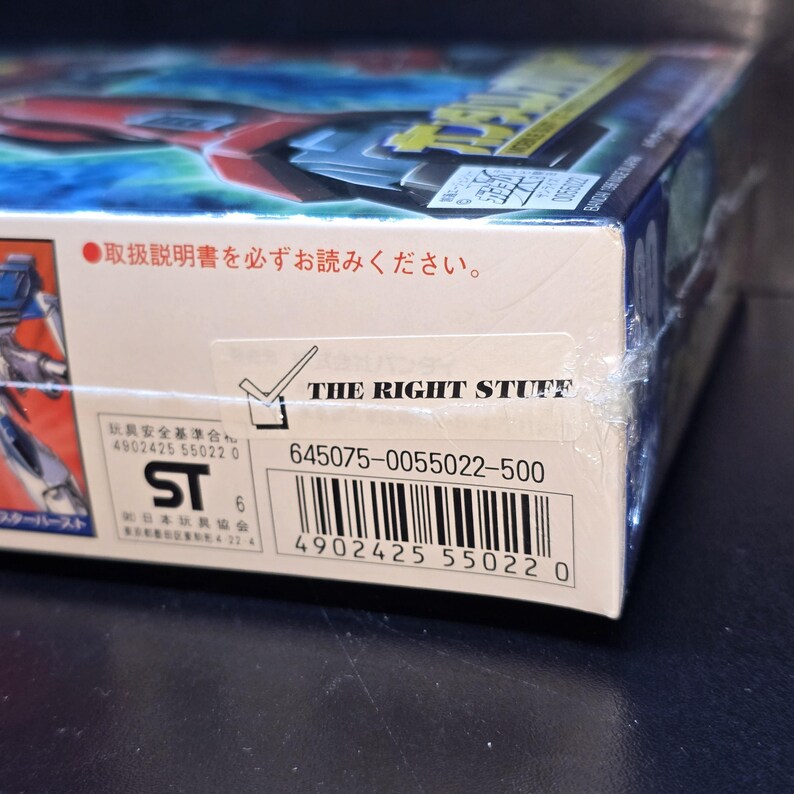 May include: A rectangular product box wrapped in clear plastic featuring a red and blue graphic on the top. The side displays a white sticker with the text THE RIGHT STUFF, a barcode, the number 645075-0055022-500, and an ST safety mark.