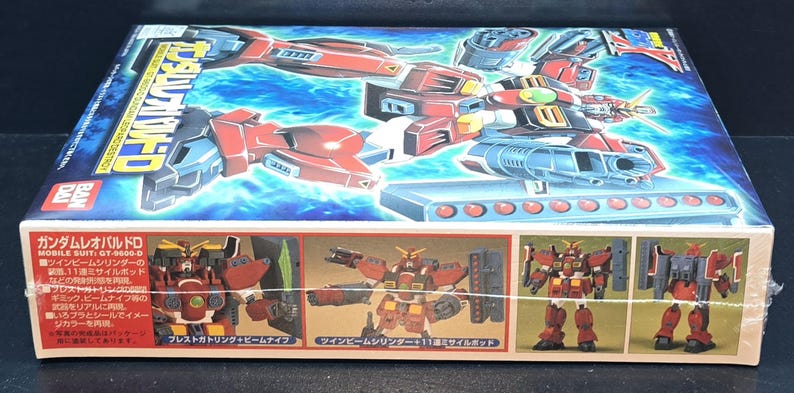 May include: A rectangular model kit box for the Gundam Leopard Destroy mobile suit. The box features a vibrant illustration of the red, white, and blue robot against a blue background, with smaller images showing the assembled figure and accessories.
