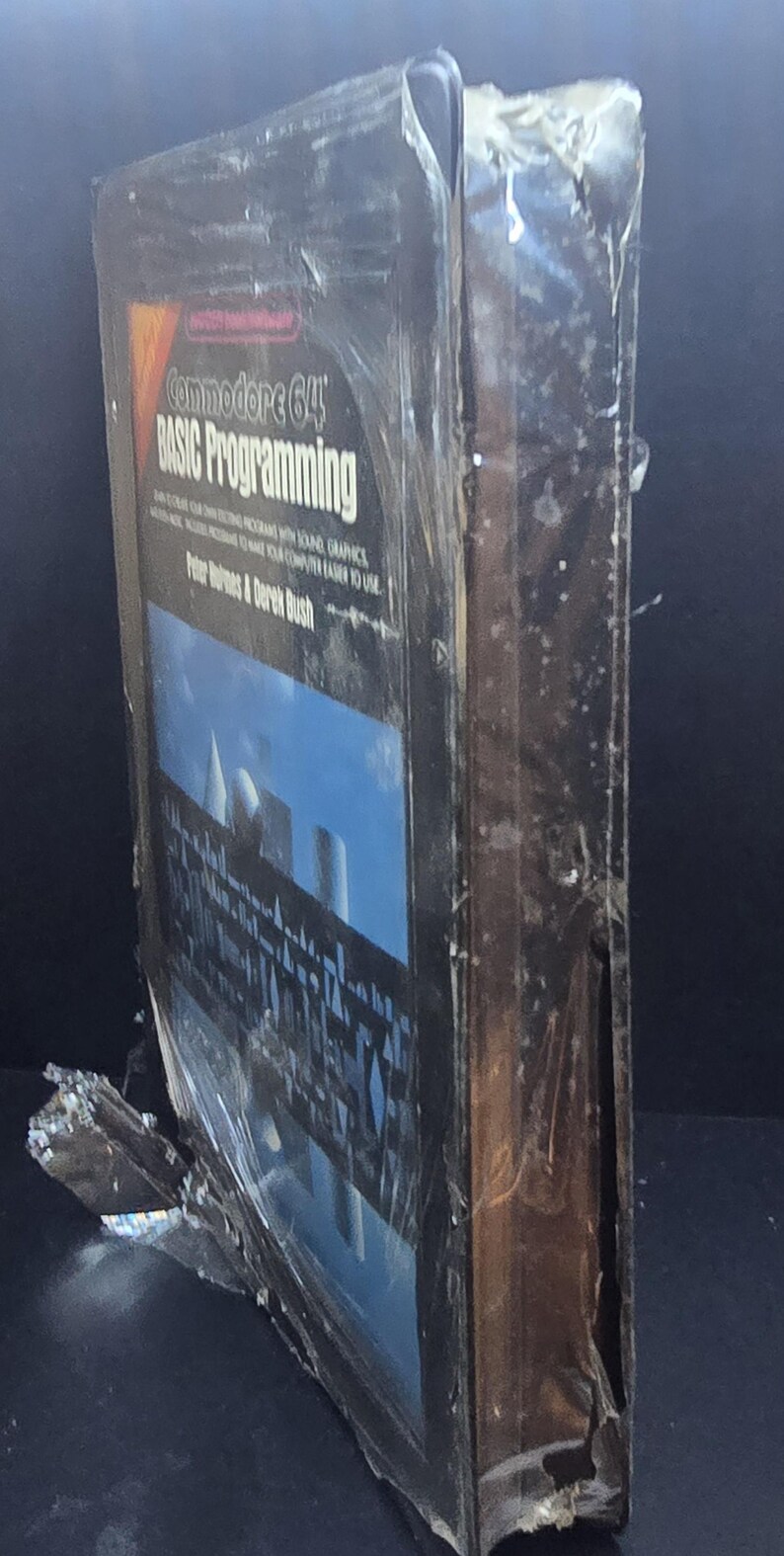 K&ouml;nnte beinhalten: Ein Commodore 64 Basic Programming Buch, noch in Plastik versiegelt. Das Cover zeigt einen blauen Himmel mit wei&szlig;en Strukturen. Das Buch ist von Peter Holmes & Derek Bush.