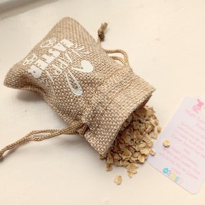 May include: A small burlap bag with a white drawstring and the text "Happy Easter" printed on it. The bag is filled with oats and is spilling out onto a white surface.