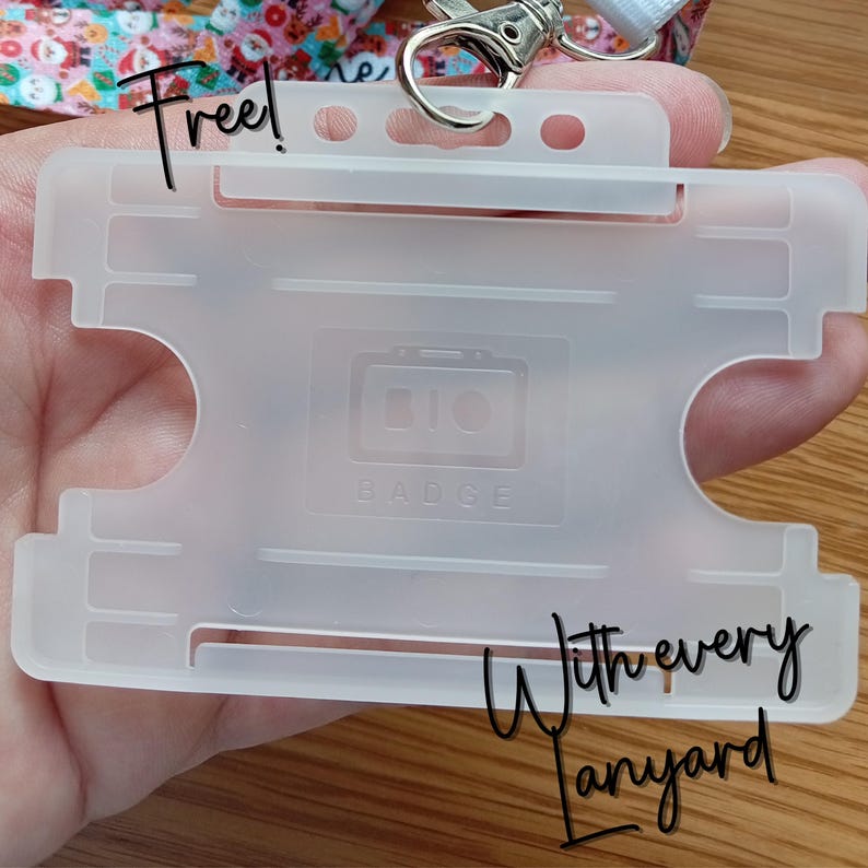 May include: A translucent, frosted plastic horizontal badge holder featuring a rectangular cutout design and a central embossed logo that reads BIO BADGE. The holder includes a top slot for a metal swivel hook attachment connected to a patterned lanyard.