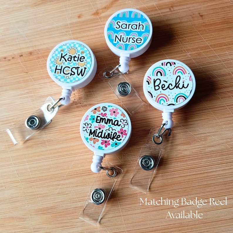 May include: Four circular white badge reels with retractable clear plastic straps and metal clips. Each reel features a unique colorful design: one with yellow flowers, one with blue rainbows, one with multicolored rainbows, and one with pink and orange flowers.