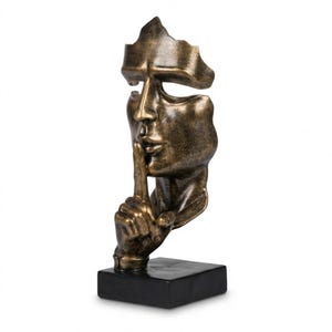 Op de afbeelding: Een bronzen sculptuur van een menselijk gezicht met een vinger voor de lippen, gemonteerd op een zwarte rechthoekige basis. Het gezicht is gedeeltelijk gefragmenteerd, wat een uniek artistiek effect creëert. Het is een decoratief item.