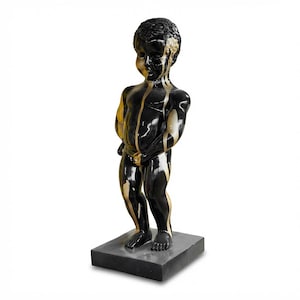 May include: A black and gold statue of a young child standing on a gray square base. The statue has a glossy finish with gold paint dripping down the front. The child's face and hair are also painted gold.