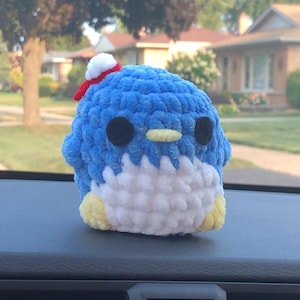 May include: A blue and white crocheted penguin plush toy with a red and white hat. The penguin has black eyes and a yellow beak.
