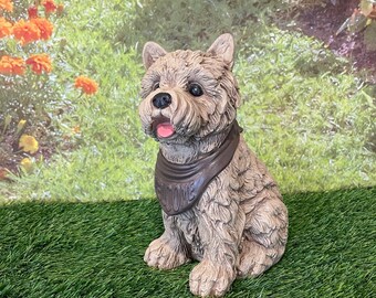 May include: A small, gray, furry dog figurine wearing a brown bandana with the word "Welcome" printed on it. The figurine is sitting on a green grassy surface.