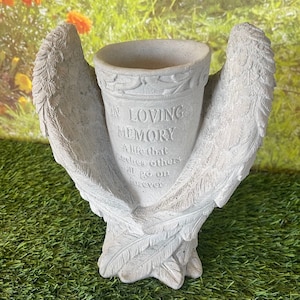 May include: A gray concrete memorial planter shaped like angel wings with the inscription "In Loving Memory A life that touches others will go on forever".