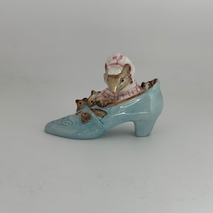 May include: A blue ceramic shoe figurine with a mother mouse and her babies inside. The mother mouse is wearing a pink and white dress and a white hat.
