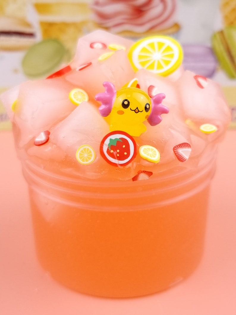 May include: Pink slime with a yellow cartoon character, strawberries, and lemon slices. The slime is in a clear plastic container.