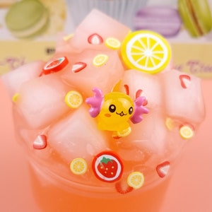 May include: A pink and white slime with a yellow cartoon character, strawberries, and lemon slices. The slime is in a clear glass jar.