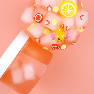 May include: A pink slime with ice cubes, lemons, and strawberries. The slime is in a clear container with a white lid.
