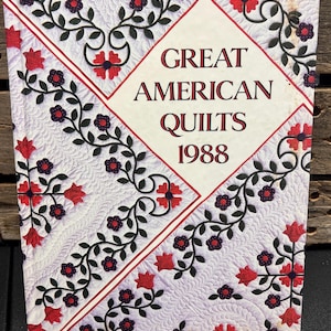 May include: A book cover titled "Great American Quilts 1988." The cover features a white background with a quilted pattern and red and black floral designs. The title is in a bold, serif font.