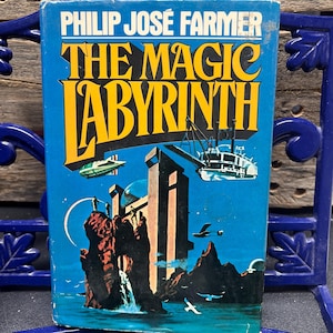 Pode incluir: Um livro de bolso vintage intitulado "THE MAGIC LABYRINTH" de Philip José Farmer. A capa apresenta um fundo azul com letras amarelas e pretas e uma ilustração de ficção científica de uma paisagem futurista com veículos voadores.