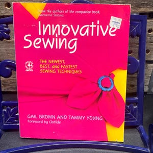 May include: A book titled "Innovative Sewing" with a bright pink cover and white text. The cover features a stylized flower and the text "The Newest, Best, and Fastest Sewing Techniques." Authors are Gail Brown and Tammy Young.