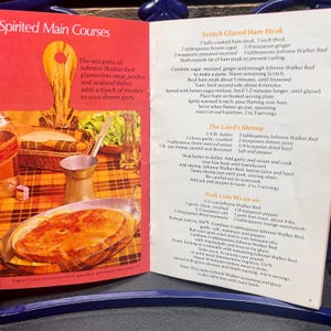 May include: Open cookbook page with recipes for Scotch Glazed Ham Steak, The Laird's Shrimp, and Pork Loin Wi-an-air. The page features a photo of a cooked ham steak in a silver dish.