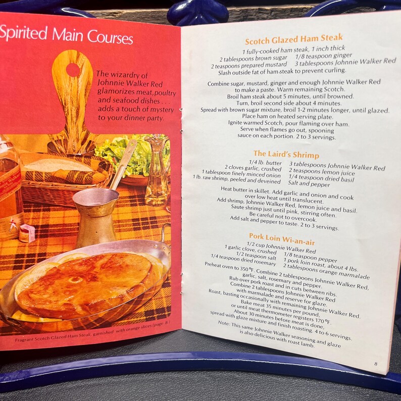 May include: Open cookbook page with recipes for Scotch Glazed Ham Steak, The Laird's Shrimp, and Pork Loin Wi-an-air. The page features a photo of a cooked ham steak in a silver dish.