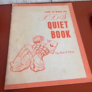 Puede incluir: Un libro de instrucciones de tapa blanda titulado How to Make an LDS Quiet Book de Ann F. Pritt. La portada es de color blanco roto con un borde color coral y presenta un dibujo lineal de un niño leyendo, impreso en tinta color coral.
