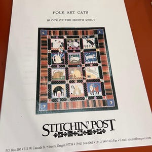 Könnte beinhalten: Ein gedrucktes Schnittmusterblatt mit dem Titel FOLK ART CATS BLOCK OF THE MONTH QUILT von STITCHIN' POST. In der Mitte ist ein Quilt-Design mit zwölf quadratischen Blöcken zu sehen, die jeweils eine andere Katzenillustration zeigen, umgeben von einem gestreiften Rand.