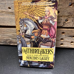 Peut inclure: Un livre de poche intitulé "Oathbreakers" de Mercedes Lackey. La couverture présente une femme à cheval avec un arc et une flèche. Le livre est le livre II: Vows and Honor.